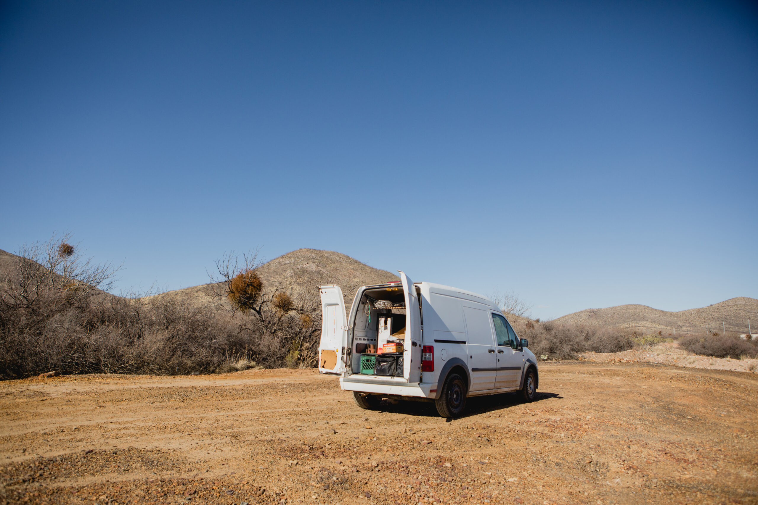 White sprinter van with rear doors open parked in desert with blue sky